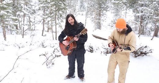 2 Men Sing In Snowfall As Wolves Creep Behind Them