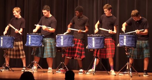 Teens Dressed In Kilts Perform Drumline Routine At Talent Show